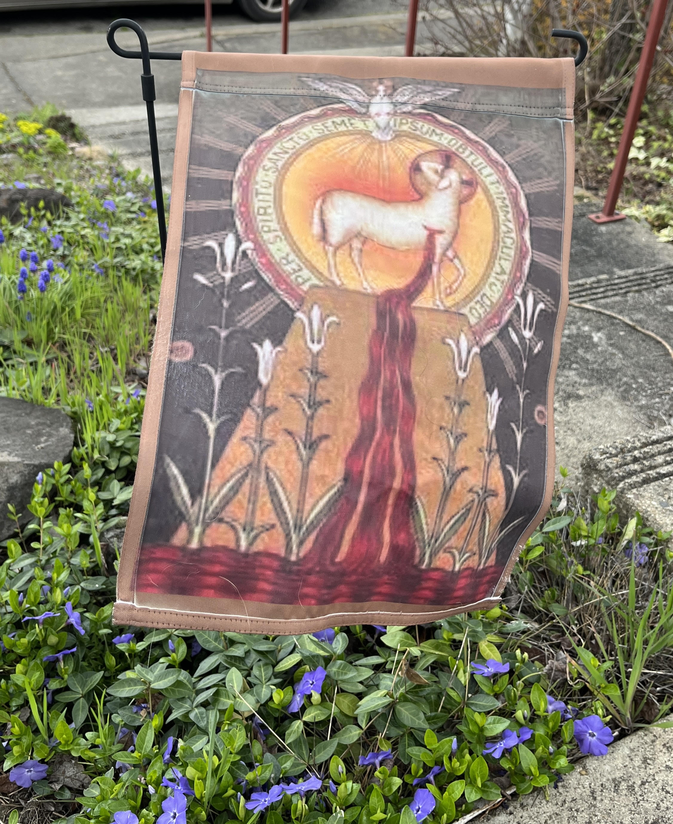 A picture of a garden flag depicting a sacrificial lamb bleeding on an altar with some Latin words, representing Jesus